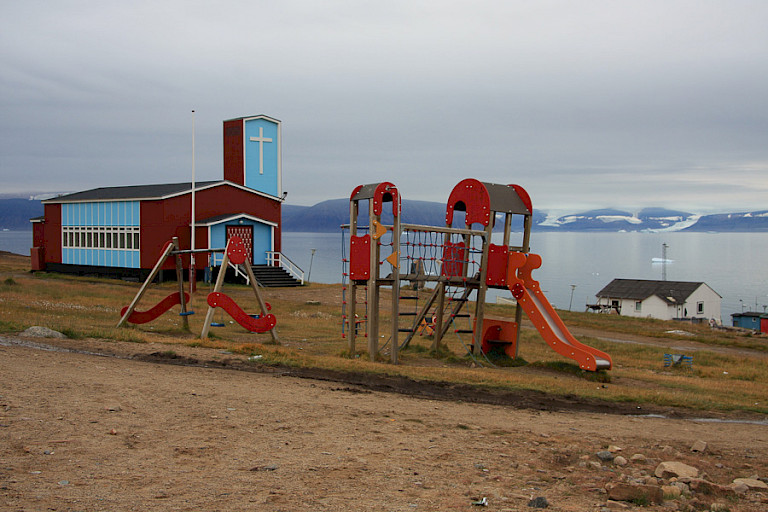 Kinderspeelplaats en kerk in Qaanaaq, Groenland.