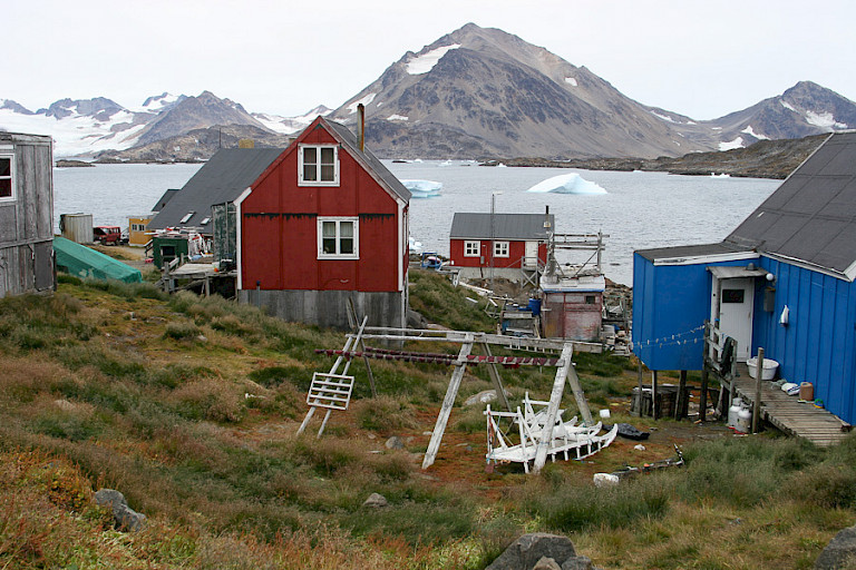 Kleurrijke huisjes langs de fjord. Rond het huis staan sleden, kajaks en droogrekken.