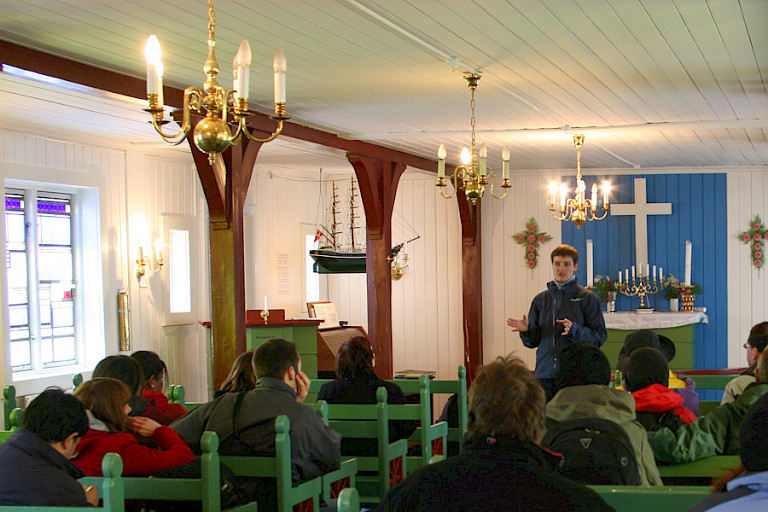 Toeristen luisteren aandachtig naar de verhalen in het sobere kerkje van Tasiilaq.