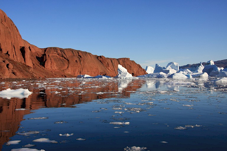Het dieprode landschap contrasteert tegen de blauwe ijsbergen.